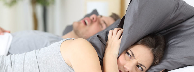 cosinuss-sleep_apnea_man-snoring-while-his-wife-is-covering-ears-with-the-pillow_410426641