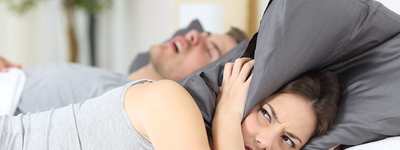 man snoring while his wife is covering ears with the pillow