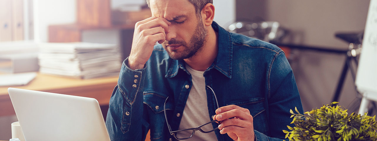 cosinuss-stress-radar-einzelbild-feeling-sick-and-tired-frustrated-young-man-massaging-his-nose-and-keeping-eyes-closed_345950645 stressed man at work