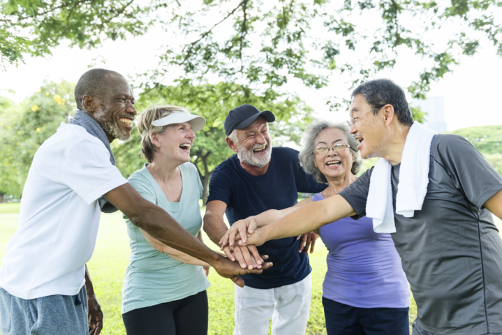 COPD physical exercise patients happy Five elderly people stand in a circle, smiling as they place their hands on top of each other in the center.