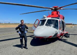 Ein glücklicher Pilot steht vor seinem rot-weißen Rettungshubschrauber.