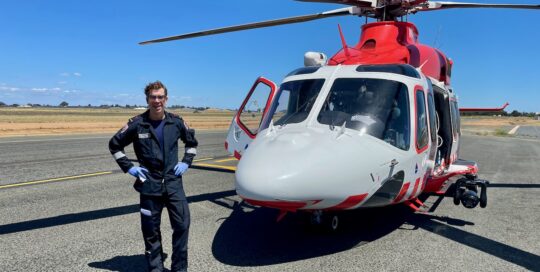 Ein glücklicher Pilot steht vor seinem rot-weißen Rettungshubschrauber.