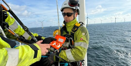 The c-med Alpha dual charging station held by a man on a wind turbine island in the sea.