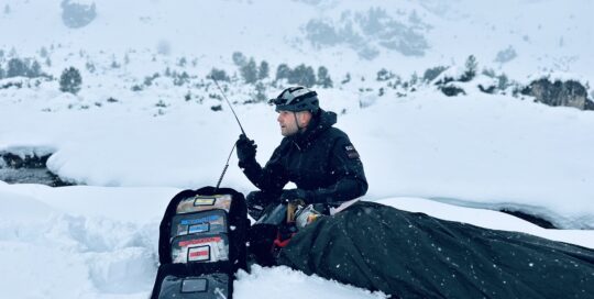Michael Helbing funkt während einer Rettung im Schnee. Der Patient ist in Decken eingewickelt, um warm zu bleiben.