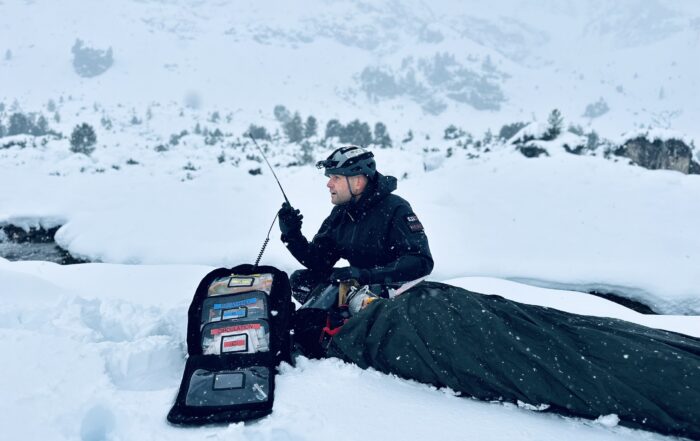 Michael Helbing funkt während einer Rettung im Schnee. Der Patient ist in Decken eingewickelt, um warm zu bleiben.